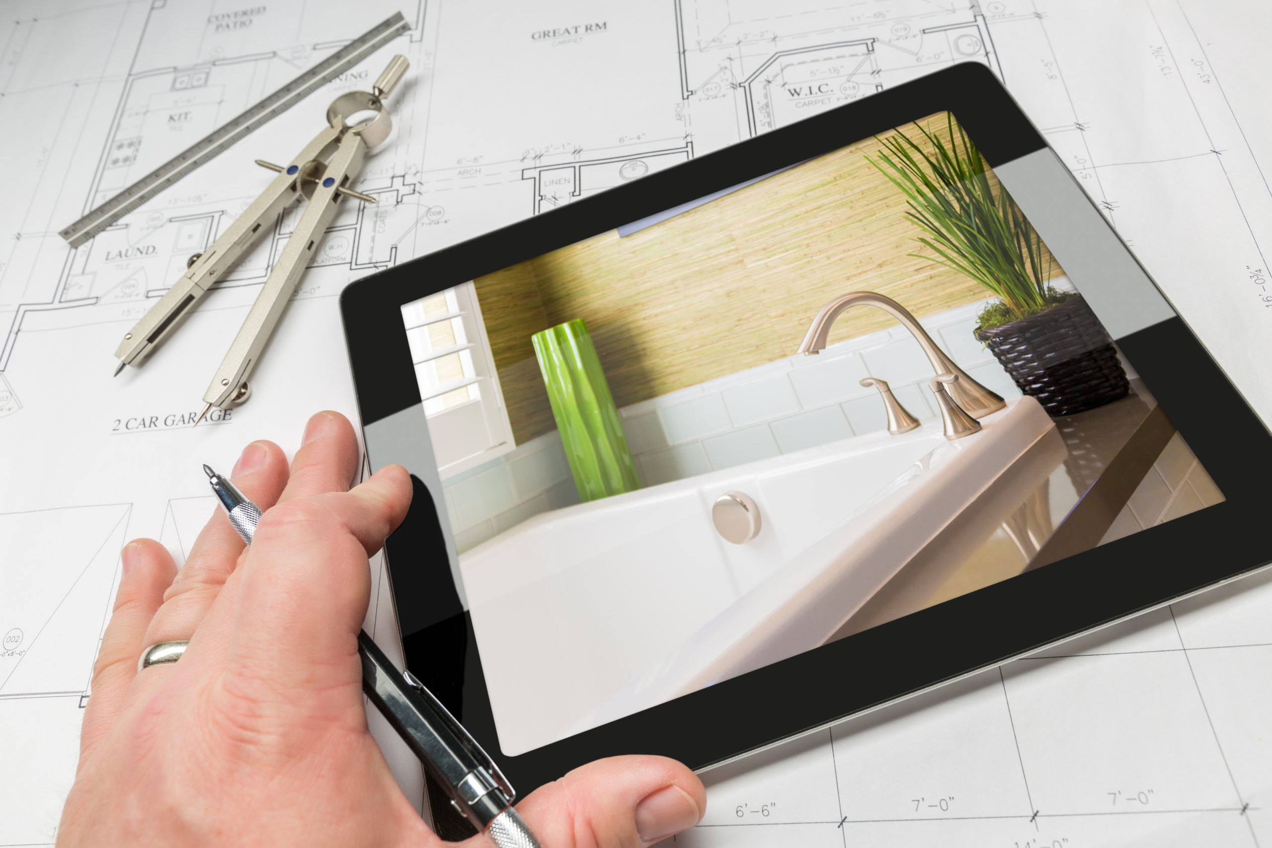 Hand of Architect on Computer Tablet Showing Luxury Bathroom Details Over House Plans, Compass and Ruler.